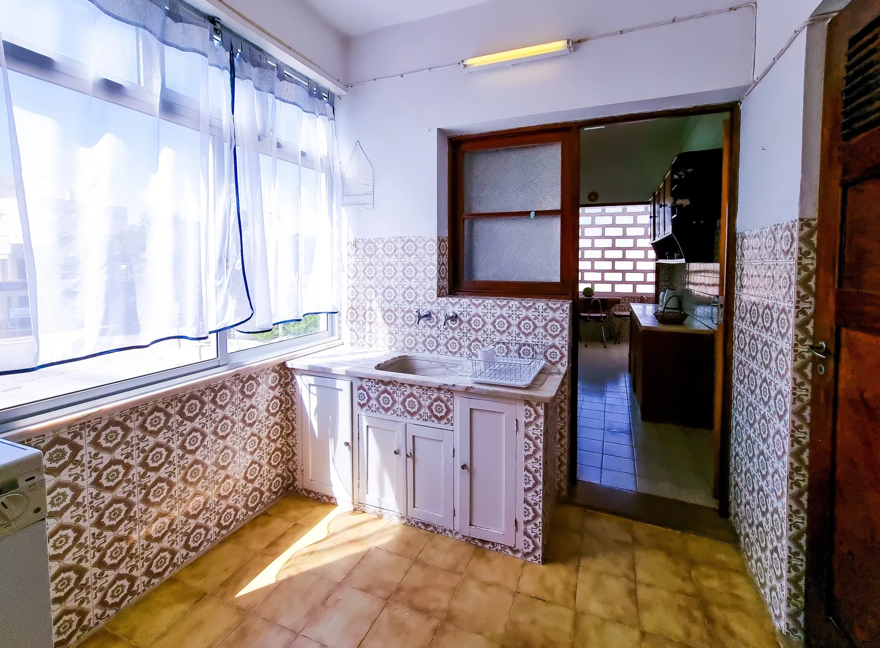 Una cocina alicatada con una encimera debajo de una ventana grande.