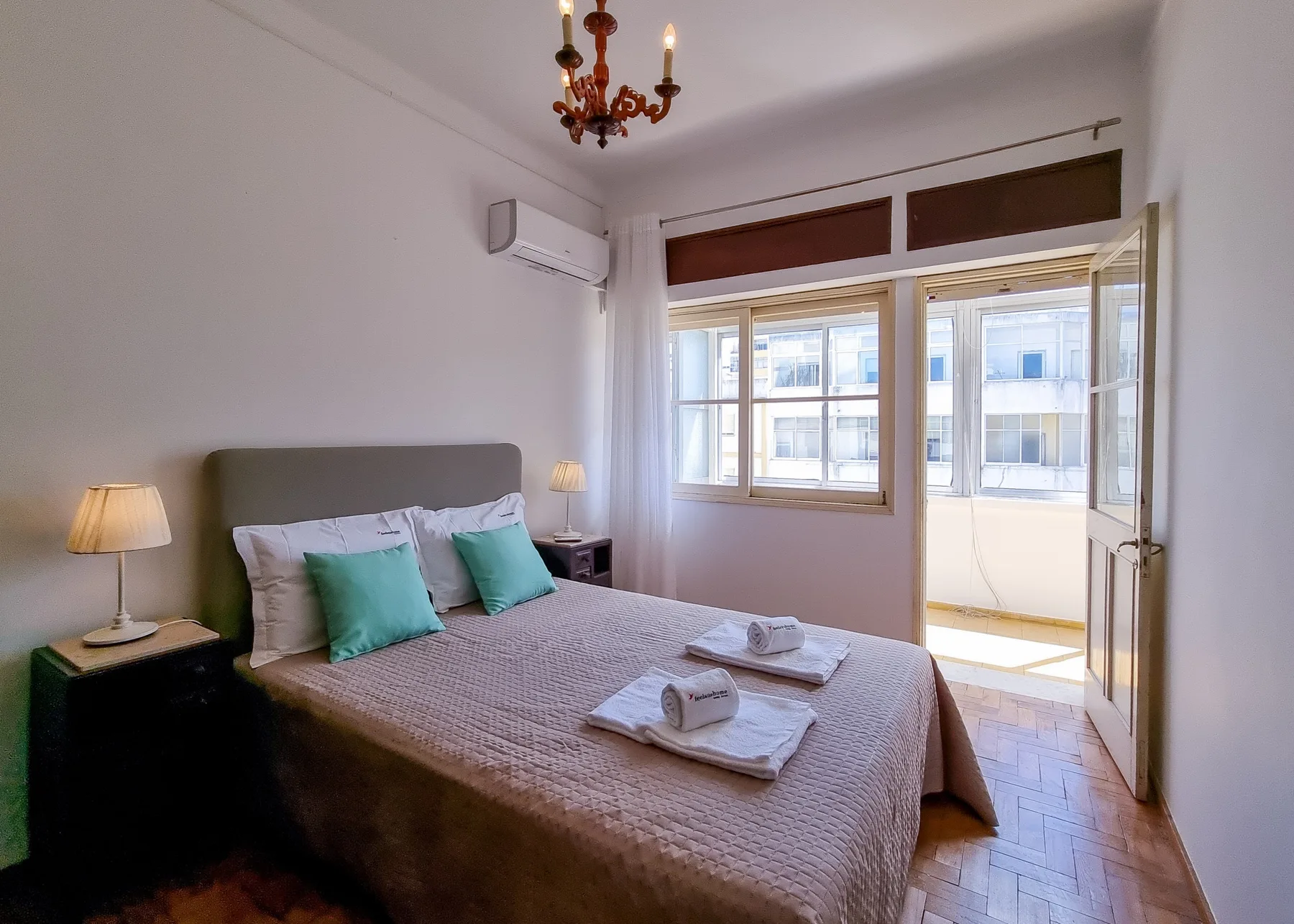 Un dormitorio con una cama, mesitas de noche y la puerta del balcón abierta.
