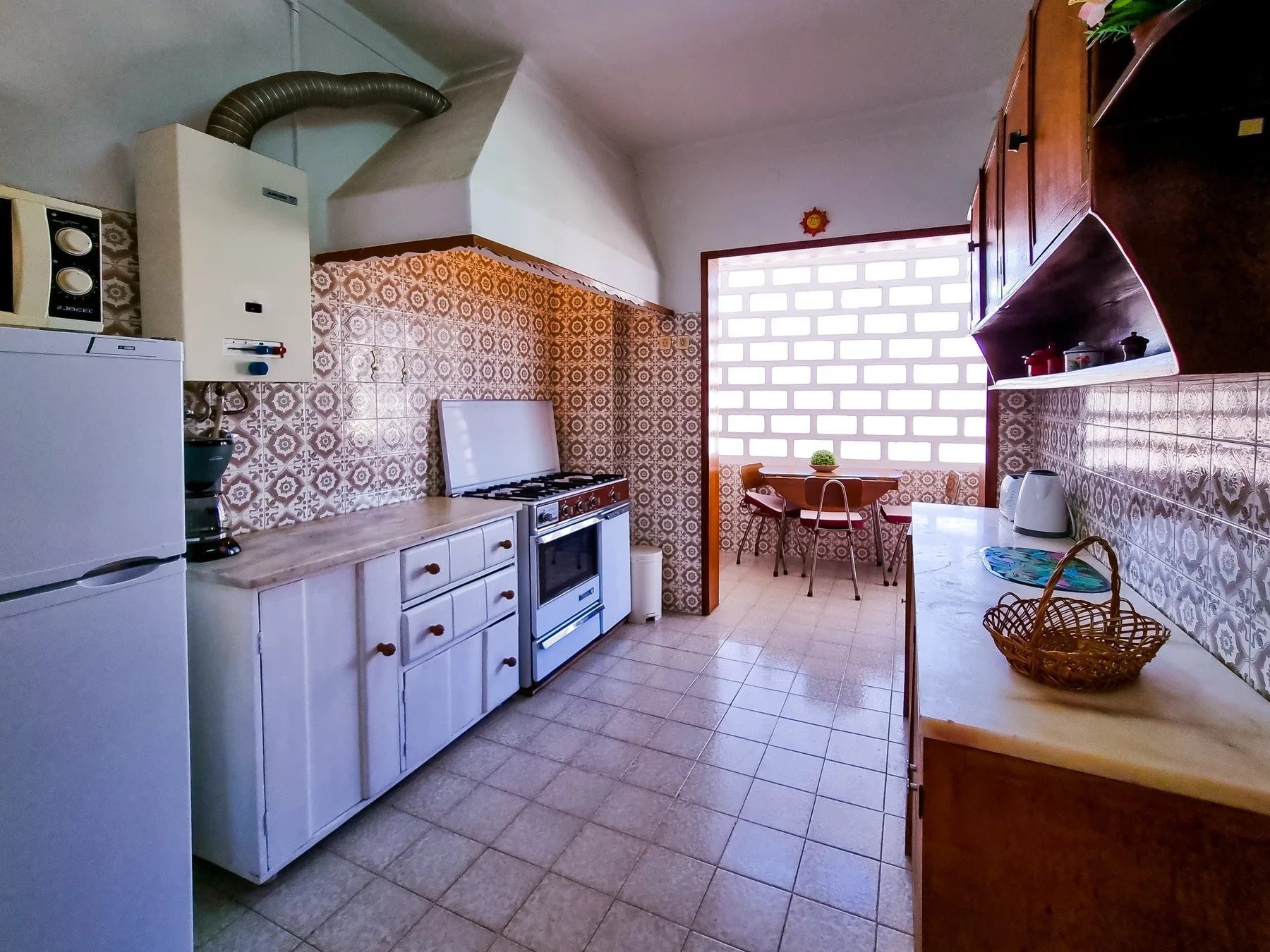 Una cocina con azulejos, refrigerador, estufa y una mesa junto a la ventana.