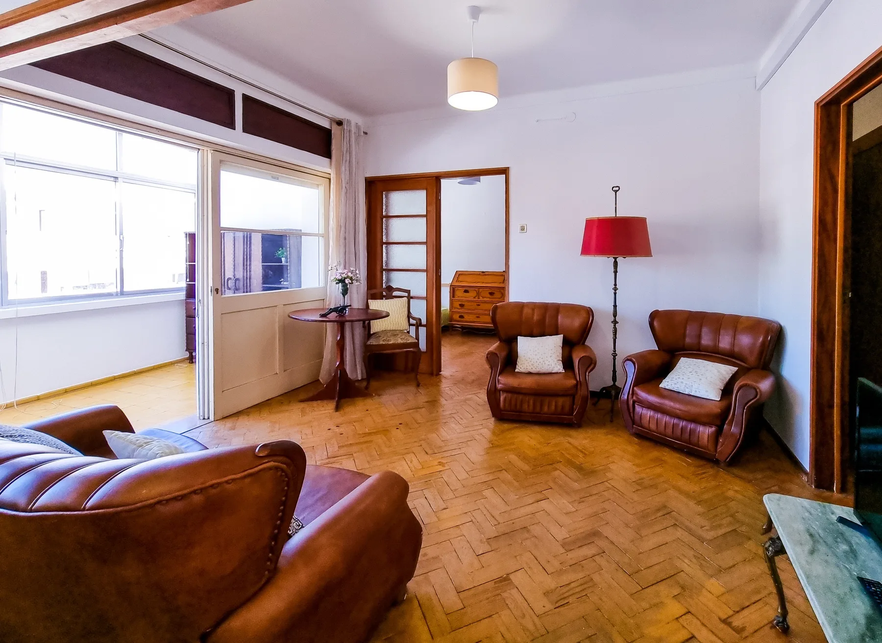Una sala de estar con asientos marrones, una lámpara de pie roja y suelo de parquet.