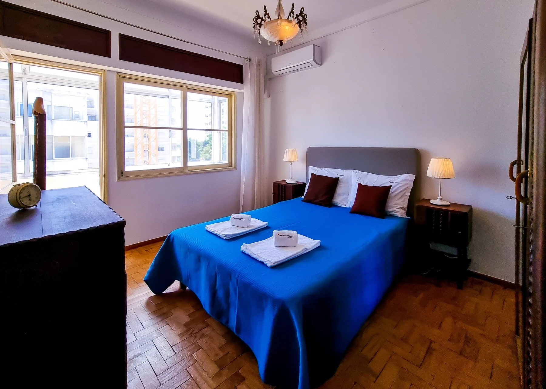Un dormitorio con una cama cubierta de azul, mesitas de noche y ventanas grandes.