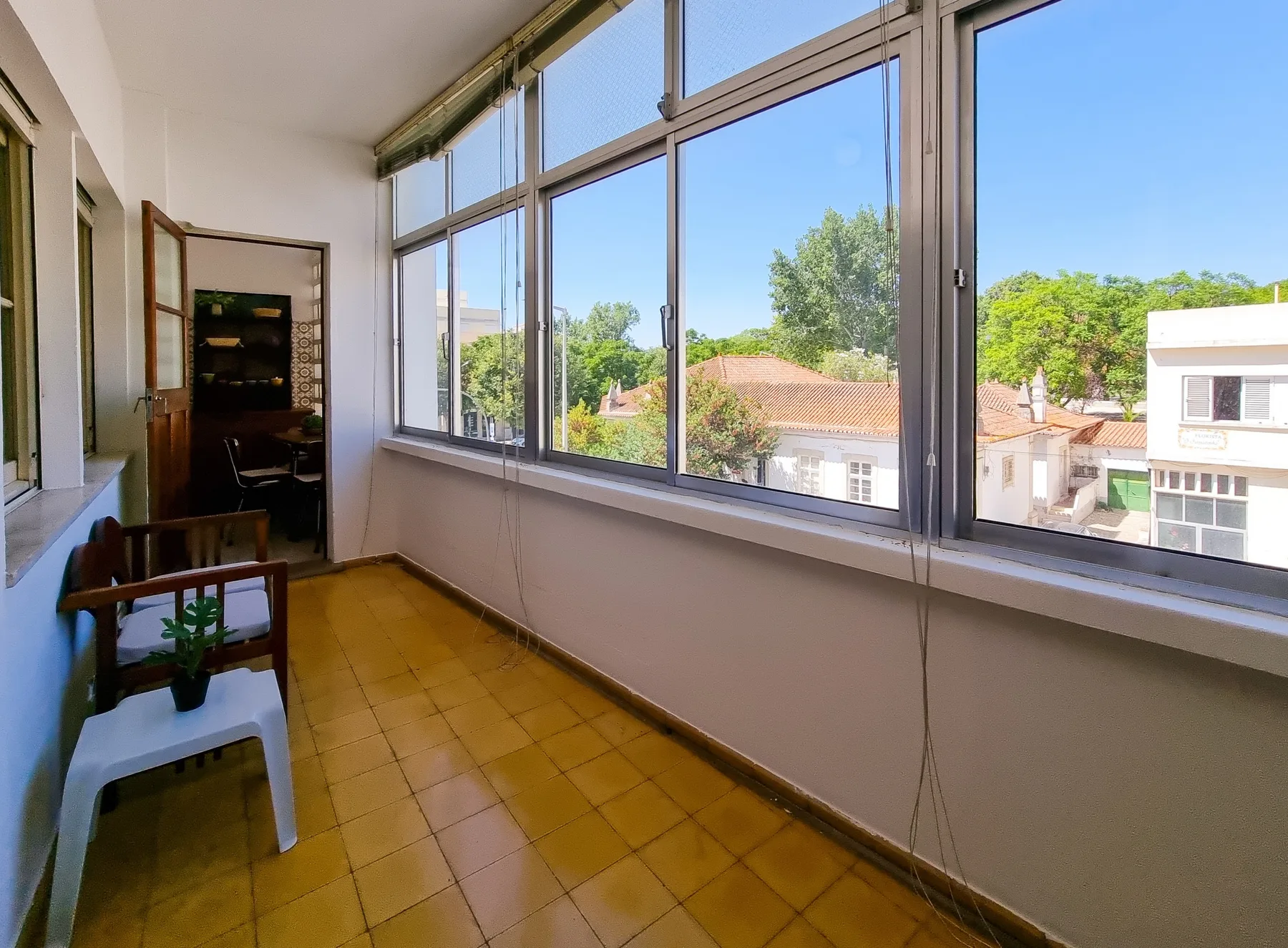 Un luminoso espacio acristalado con grandes ventanas que dan a árboles y edificios cercanos.