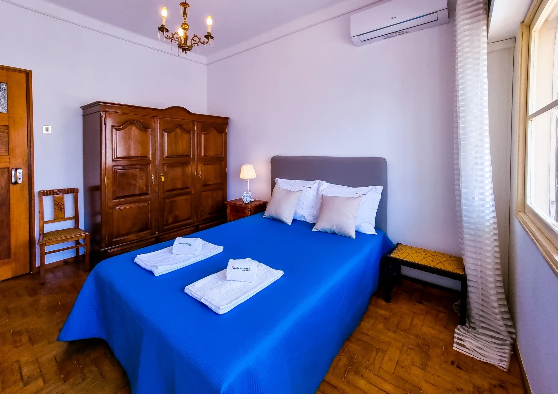 Un dormitorio con ropa de cama azul, un armario de madera y una ventana.