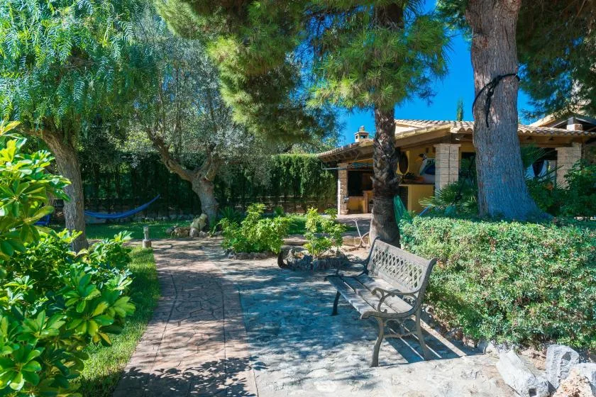 A garden patio with a paved path, bench, trees, and a covered seating area.