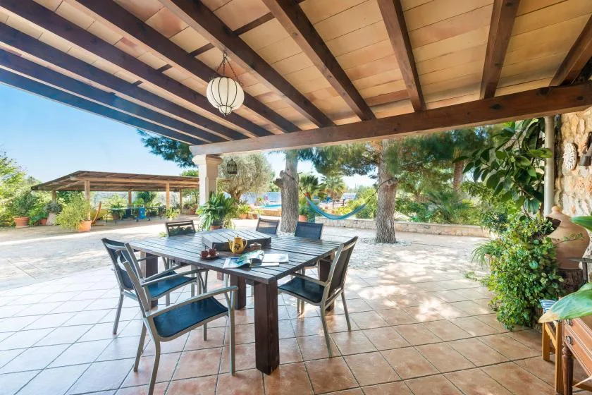 A covered patio dining area opens onto a garden with a hammock.