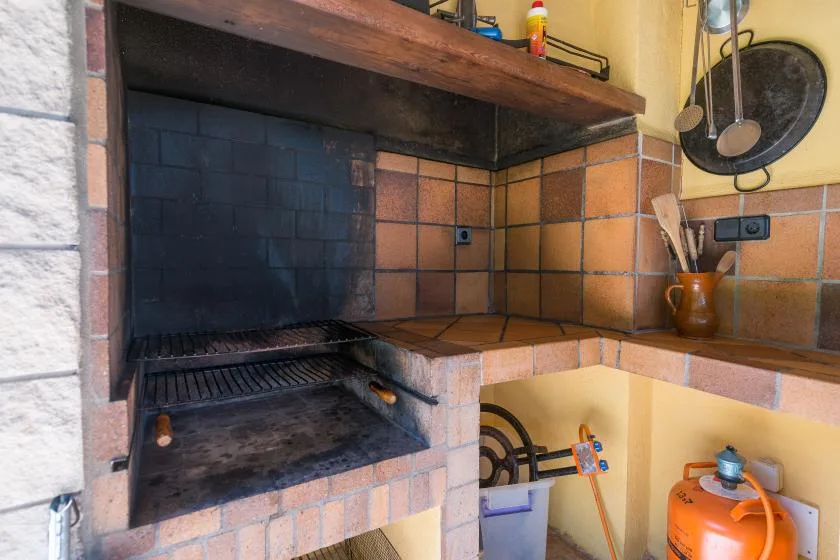 A brick barbecue grill is set into a tiled outdoor cooking area.