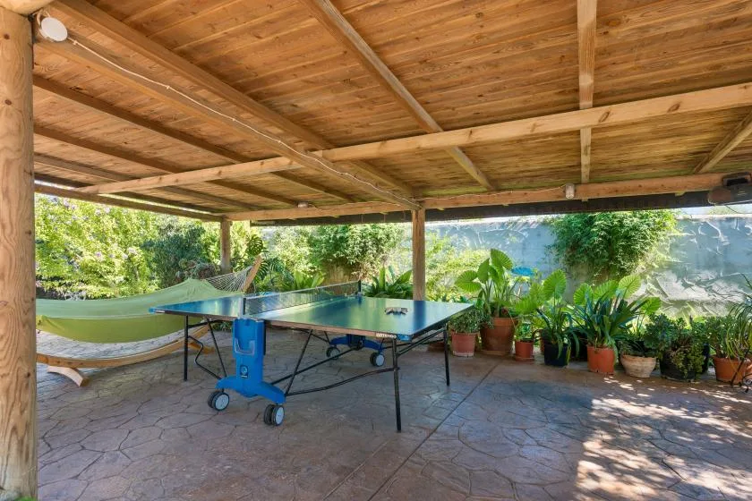A covered outdoor recreation area with a table tennis table and potted plants.