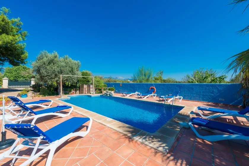 An outdoor swimming pool is surrounded by sun loungers on a tiled terrace.