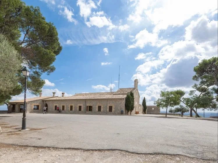 A low stone building stands beside an open paved courtyard under a blue sky.