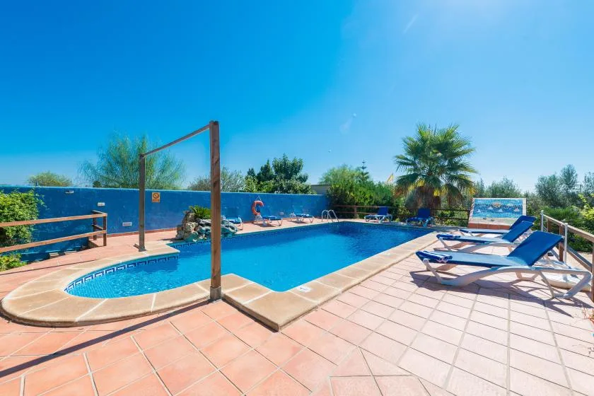 An outdoor swimming pool with lounge chairs on a tiled patio.