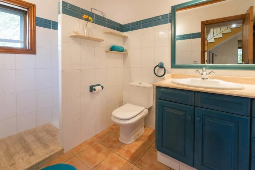 A tiled bathroom with a toilet, vanity, and small window.