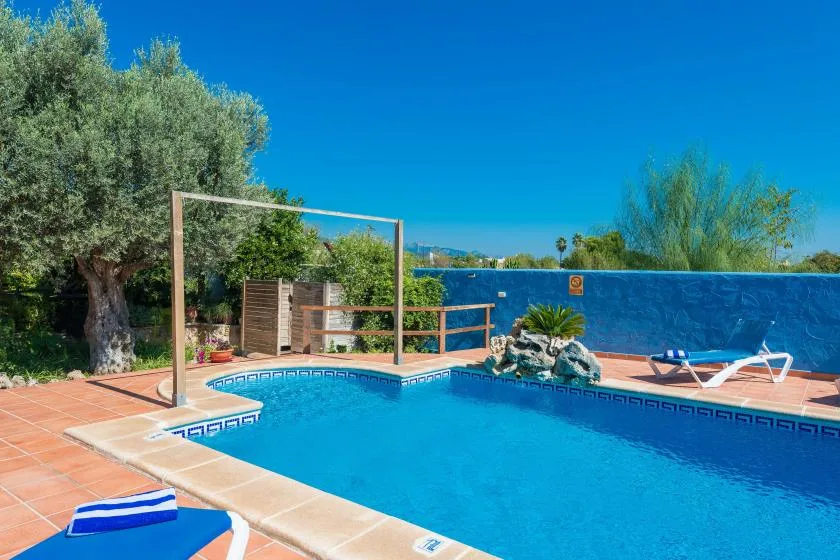 An outdoor swimming pool bordered by terracotta-colored paving and lounge seating.