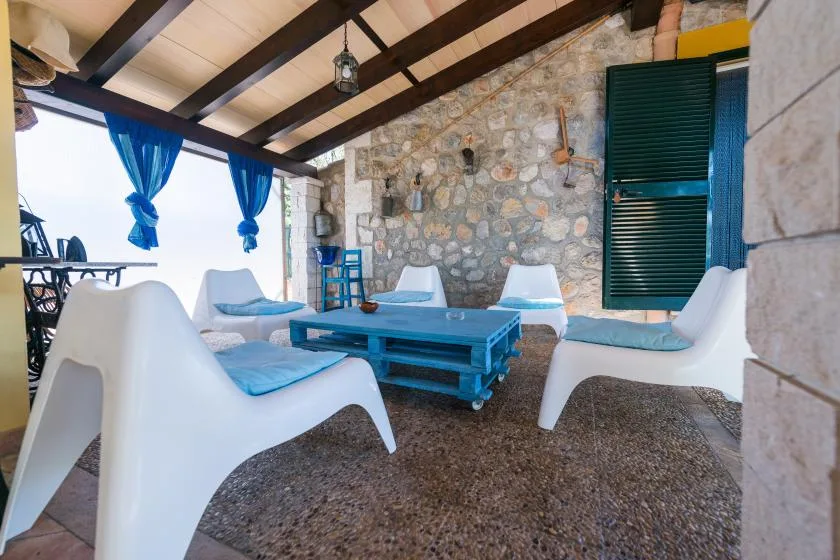 A covered outdoor seating area with a blue table and white chairs.