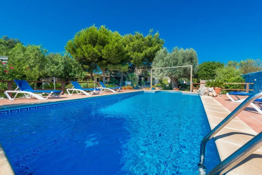 An outdoor swimming pool is surrounded by lounge chairs and greenery.