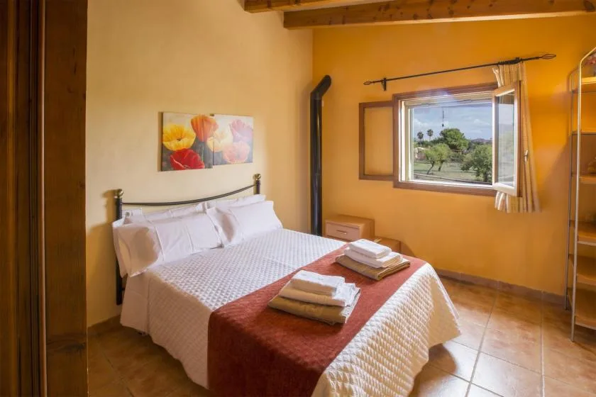 A bedroom with a neatly made bed and an open window overlooking greenery.