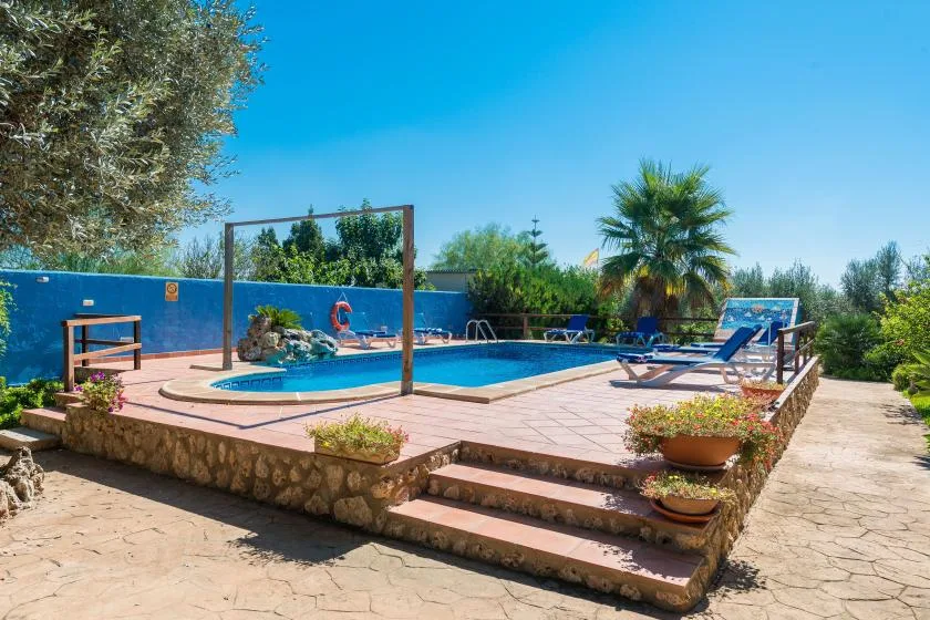 An outdoor swimming pool is surrounded by a tiled deck and greenery.