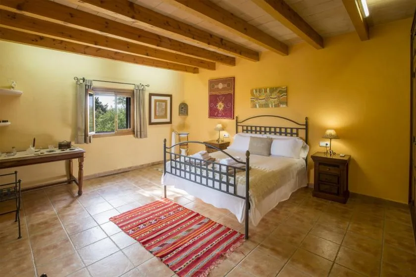 A bedroom with a metal bed, wooden ceiling beams, and a colorful rug.