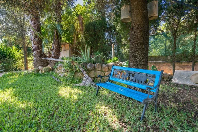A garden seating area with a bright blue bench beneath leafy trees.