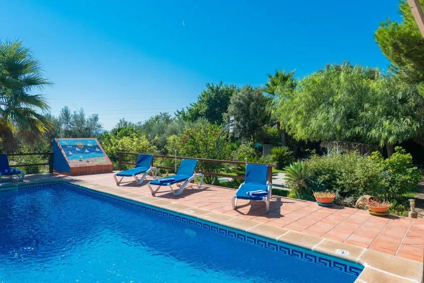 An outdoor swimming pool is bordered by a tiled deck and blue loungers.