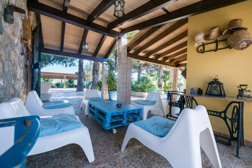 A covered outdoor seating area has white lounge chairs around a blue table.