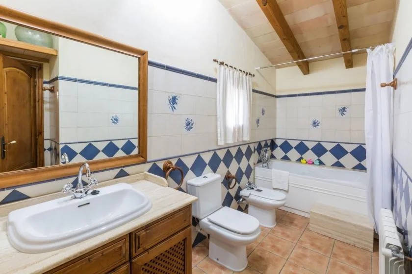A tiled bathroom with a sink, toilet, and bathtub beneath a sloped ceiling.