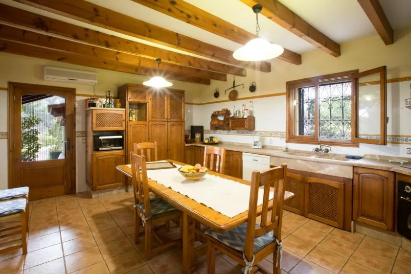 A rustic kitchen with wooden cabinets, a dining table, and exposed ceiling beams.