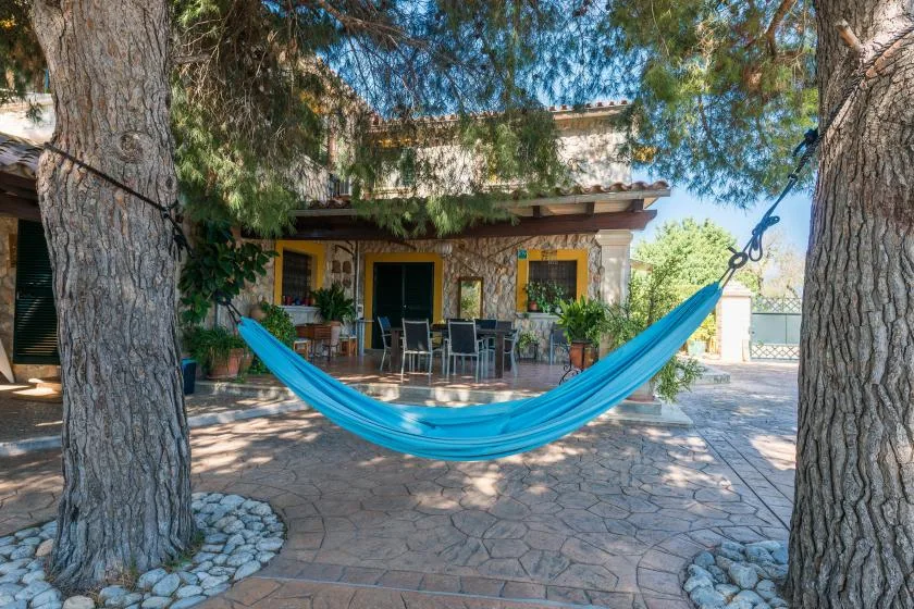 A shaded patio with a blue hammock and outdoor seating beneath trees.