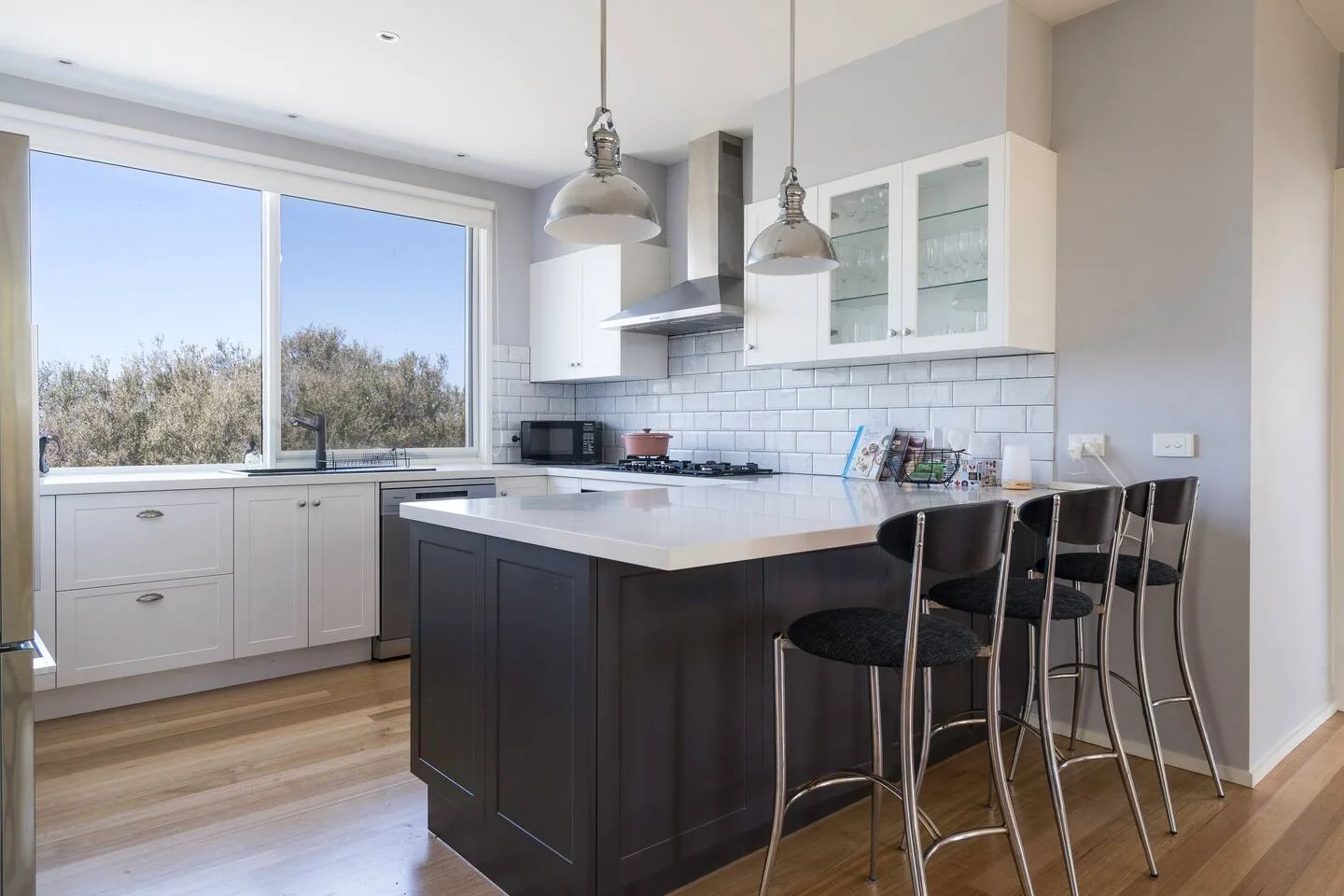 Una cocina luminosa con una isla central y grandes ventanas con vistas a los árboles.