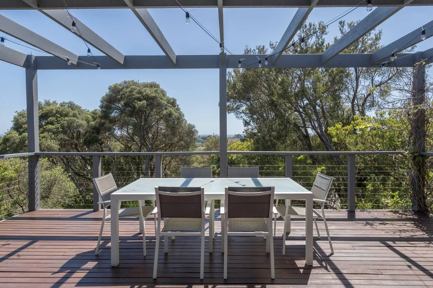 Un comedor al aire libre bajo una pérgola ofrece vistas a árboles frondosos.