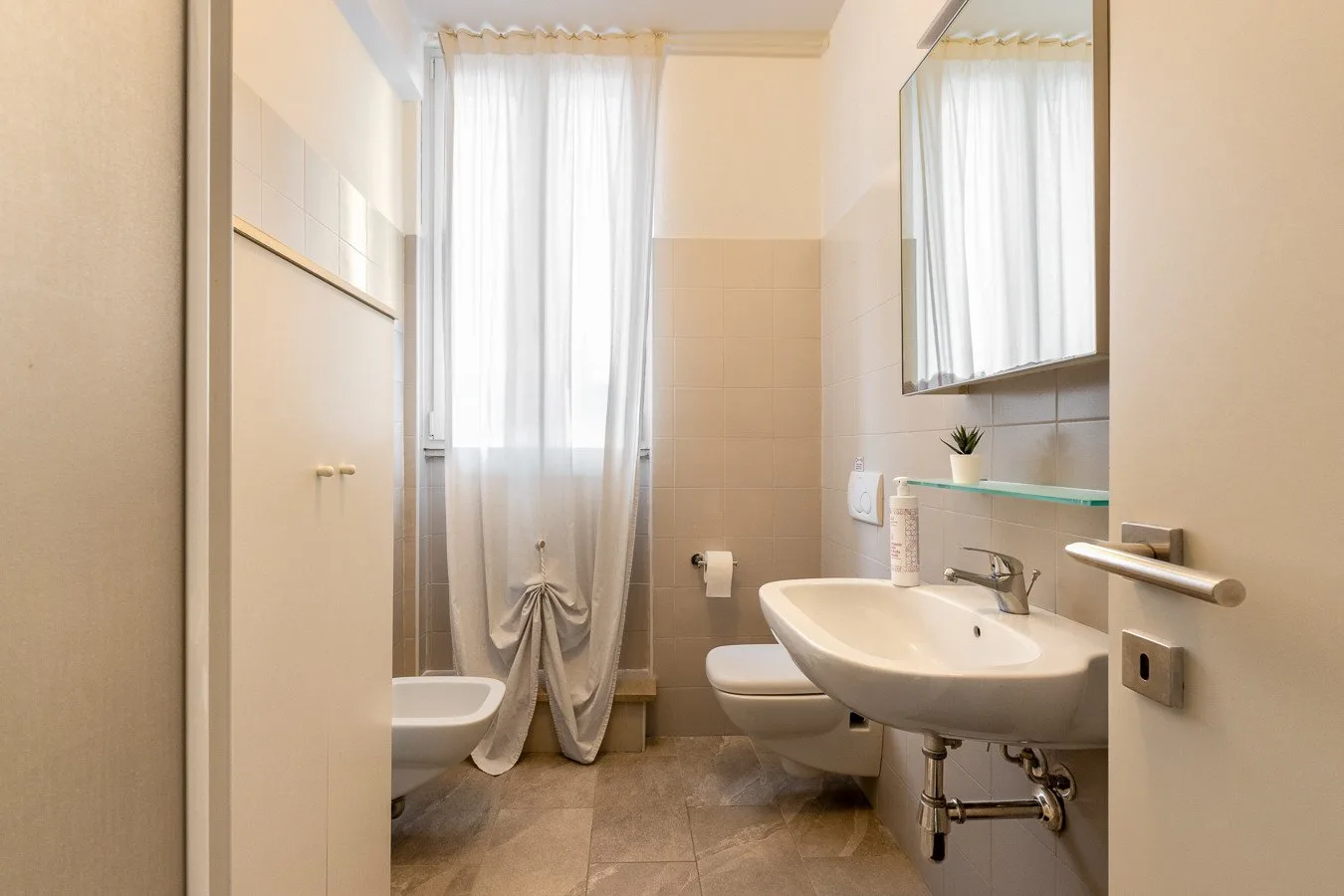 Un baño luminoso con inodoro, lavabo y una ventana con cortinas.