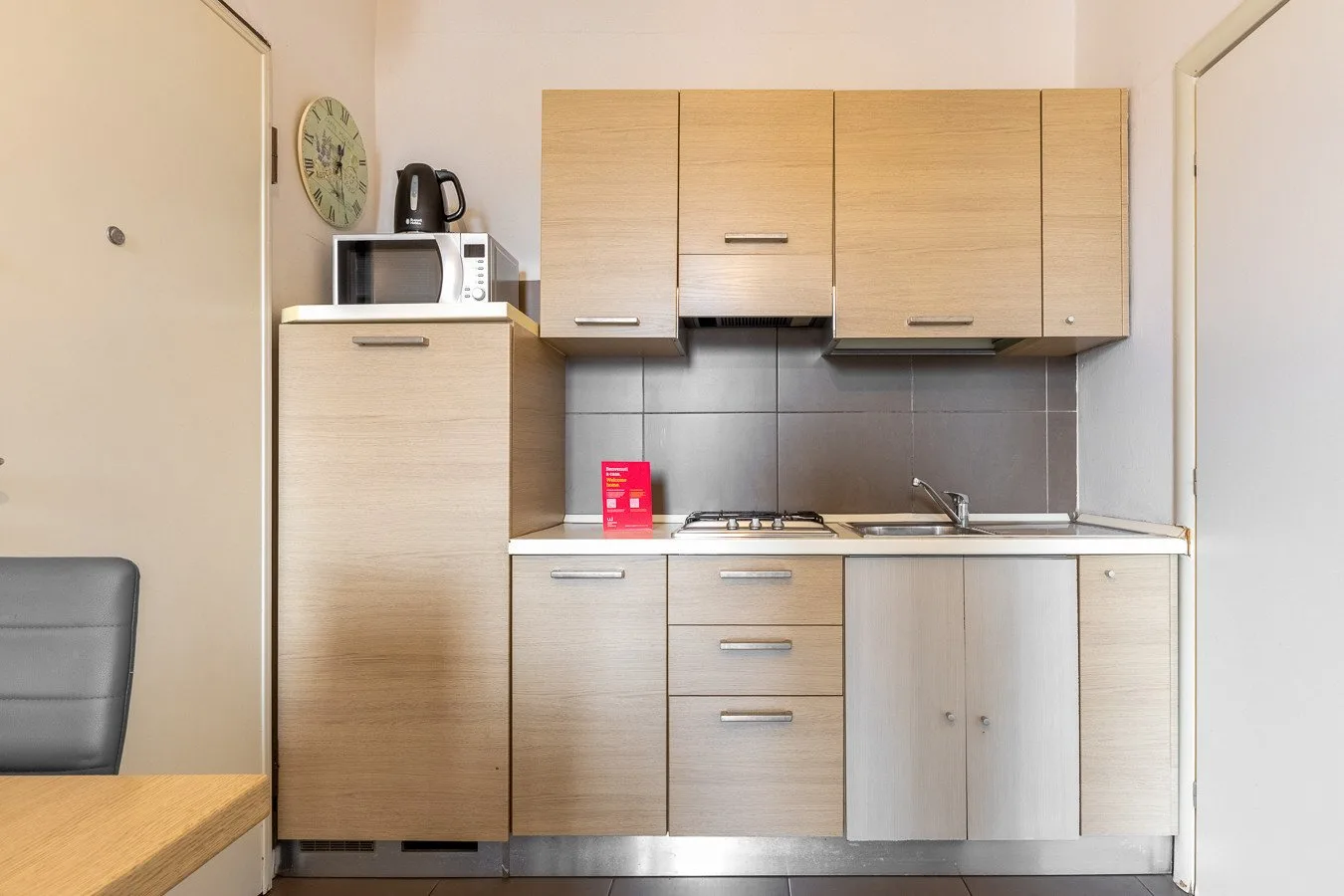 Una cocina compacta con gabinetes de madera clara, una encimera y un fregadero.
