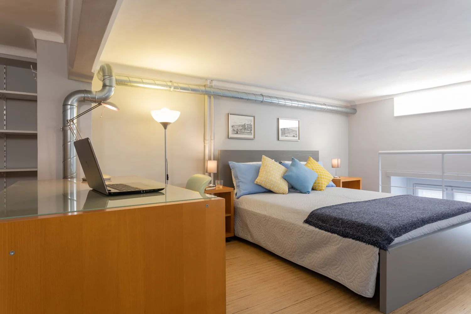 Un dormitorio con una cama, almohadas de colores y un escritorio con una computadora portátil abierta.