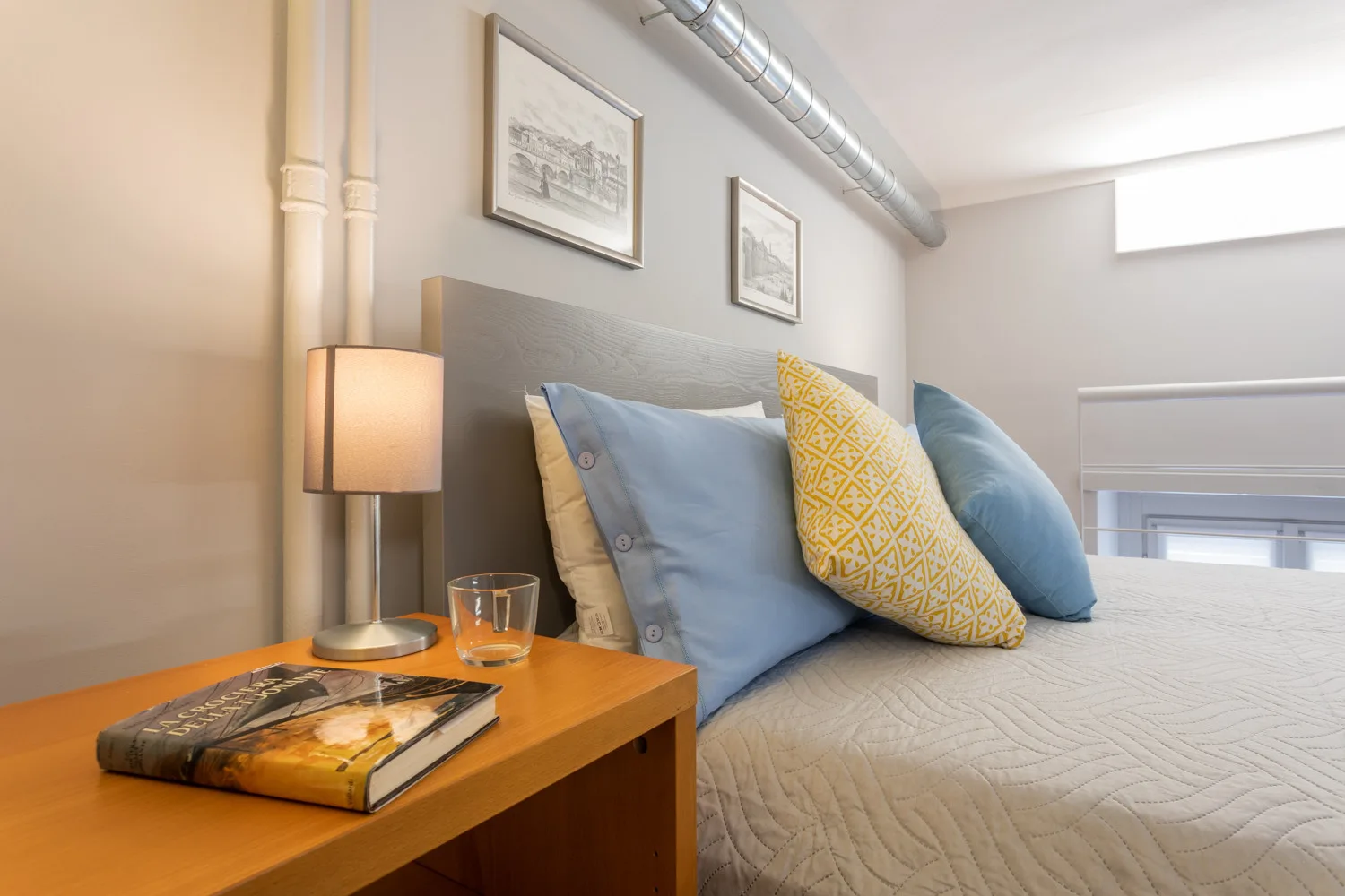 Un dormitorio con una cama tendida, almohadas de colores y una mesita de noche.