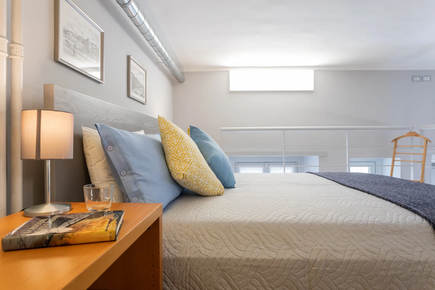 Dormitorio con una cama tendida y almohadas junto a una lámpara de noche encendida.