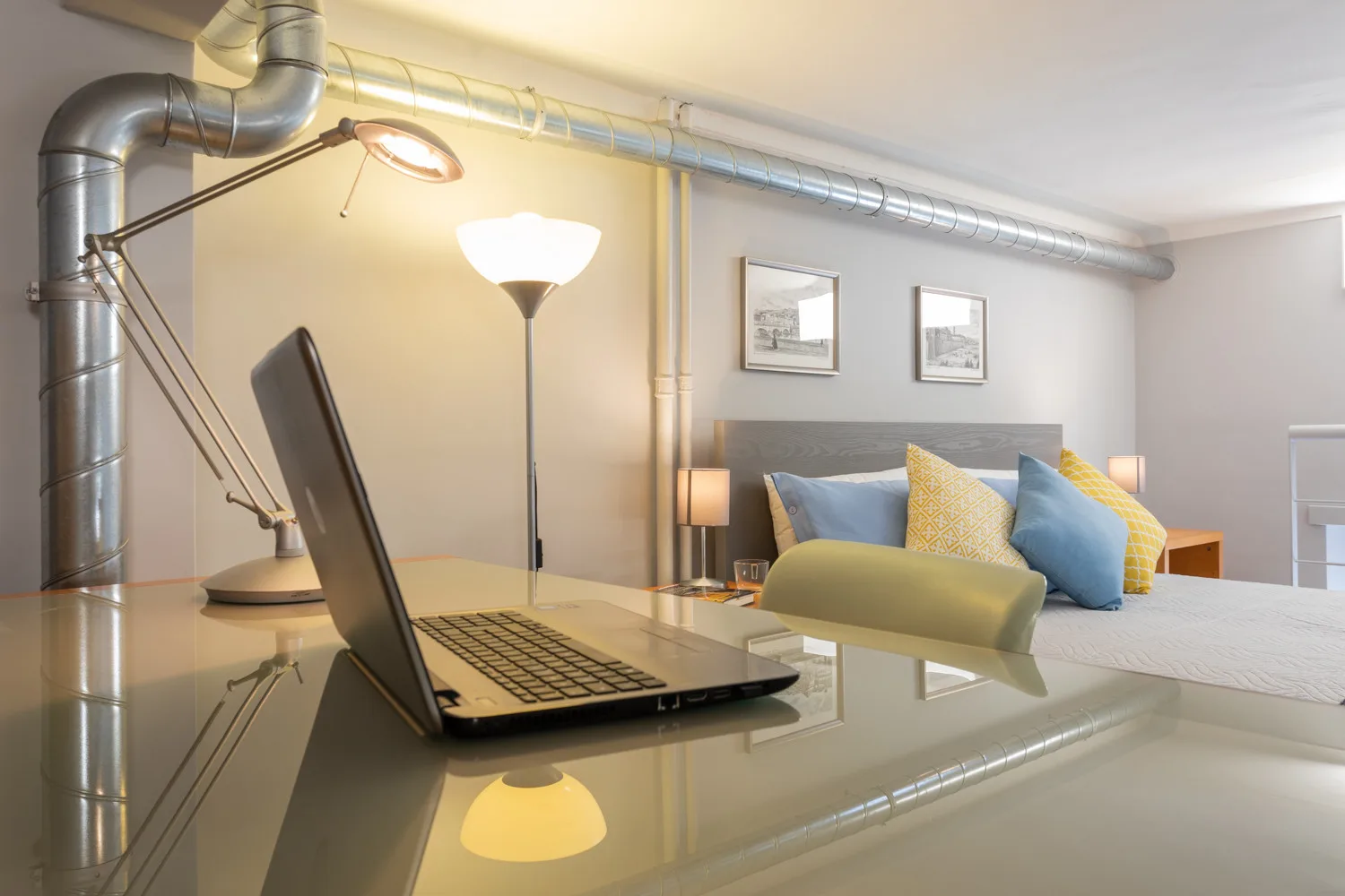 Dormitorio con una computadora portátil sobre un escritorio de vidrio en primer plano.