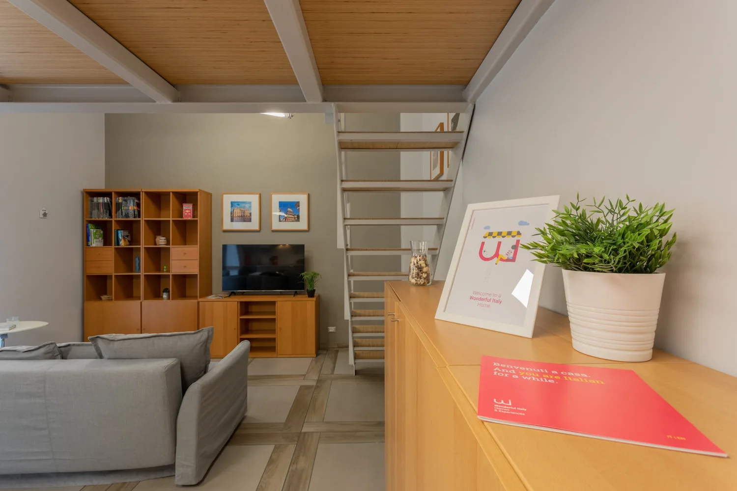 Una sala de estar con asientos, un televisor y una escalera hacia un altillo.