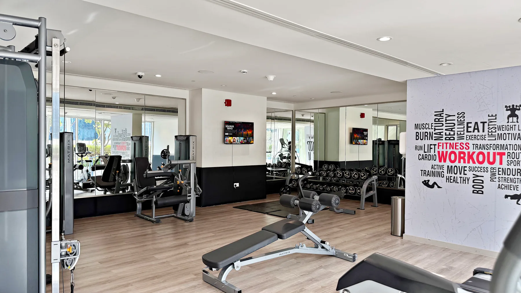 Un gimnasio luminoso con equipos de pesas, espejos y grandes ventanales.