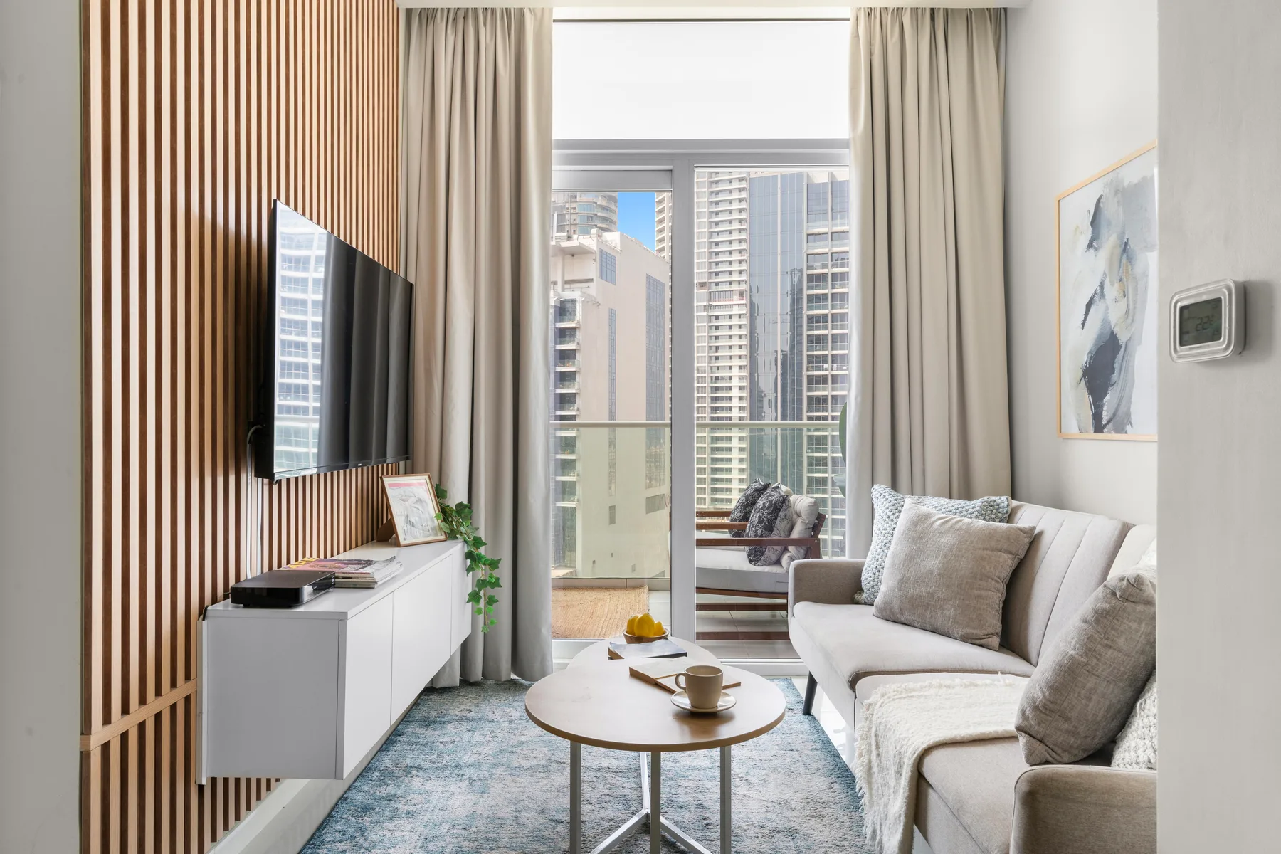 Una sala luminosa con zona de estar, mesa de centro y grandes ventanas con vistas a edificios de la ciudad.