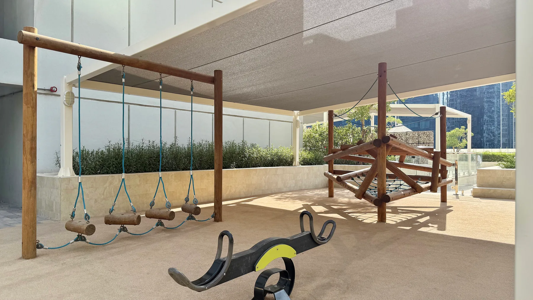 Una zona de juegos exterior cubierta tiene columpios de madera y un balancín.