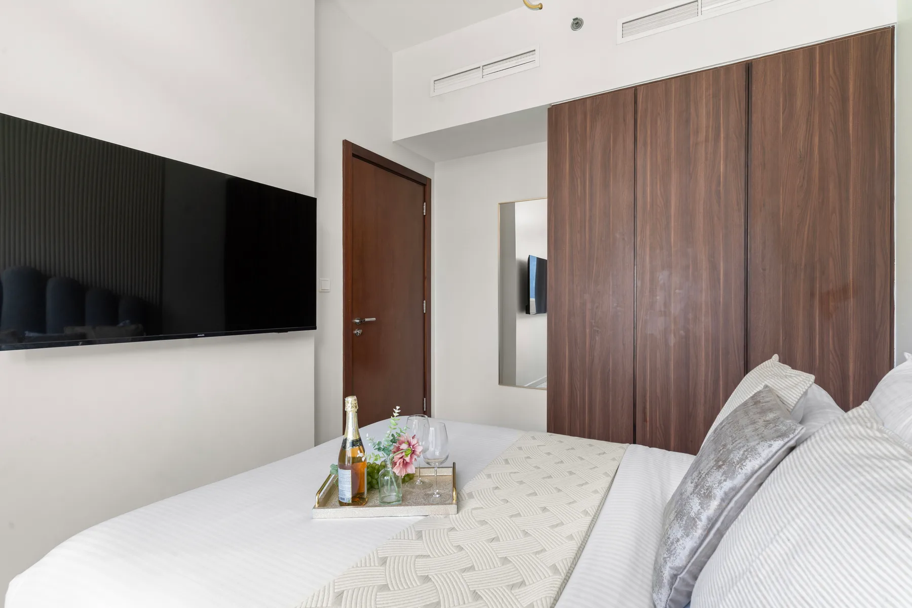 Un dormitorio con un televisor montado en la pared y una cama junto a una pared revestida de madera.