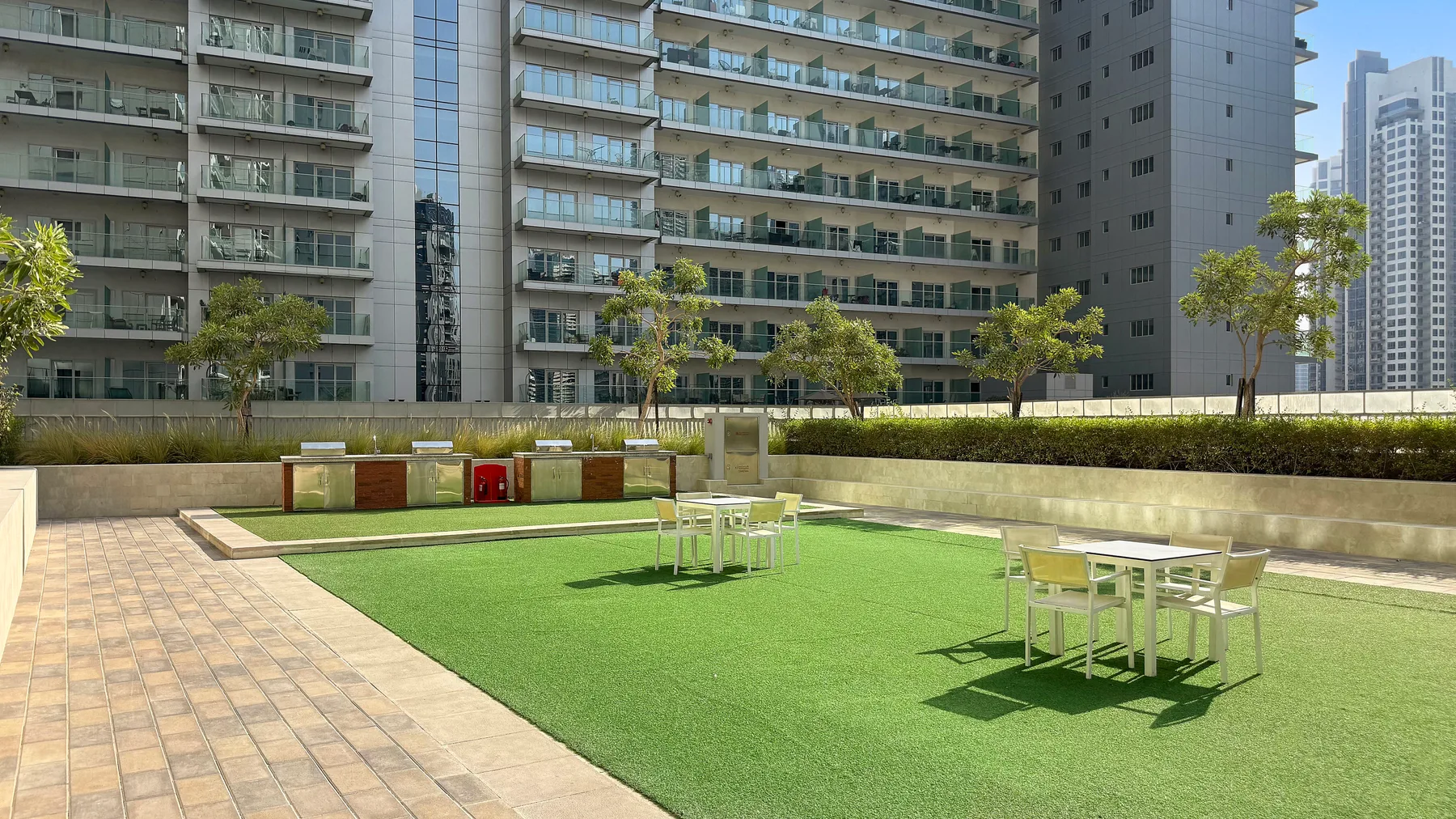 Un patio exterior con césped artificial verde y mesas con asientos entre edificios de apartamentos.
