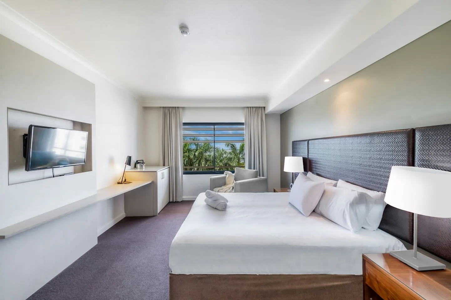 A bedroom with a bed, bedside lamps, and a mounted television.