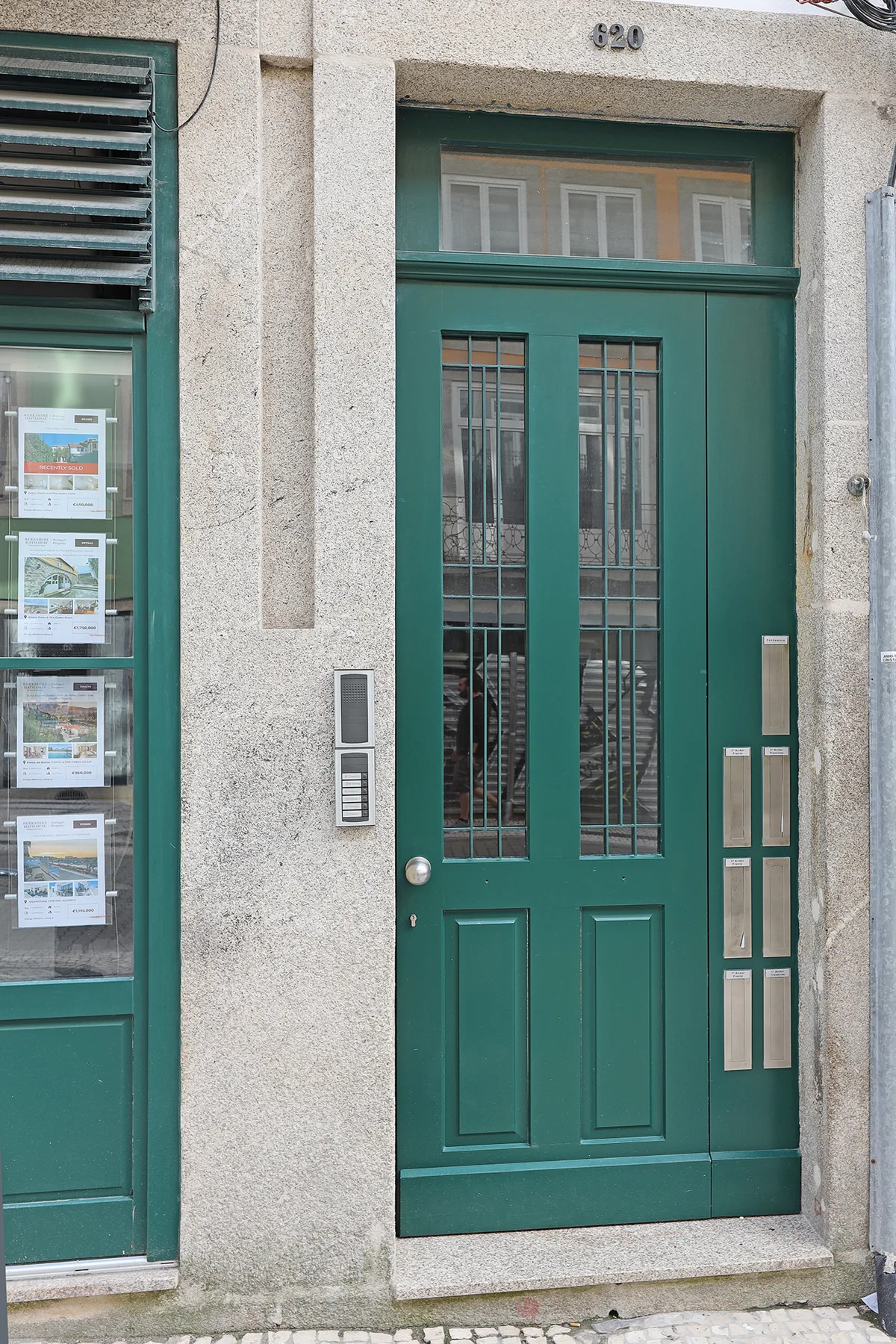 Una puerta verde con paneles de vidrio está en una fachada de piedra clara.