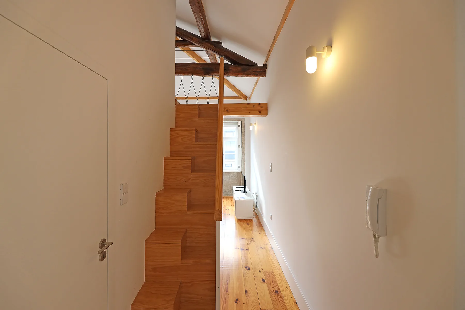 Un pasillo interior estrecho con escaleras de madera y una luz de pared.
