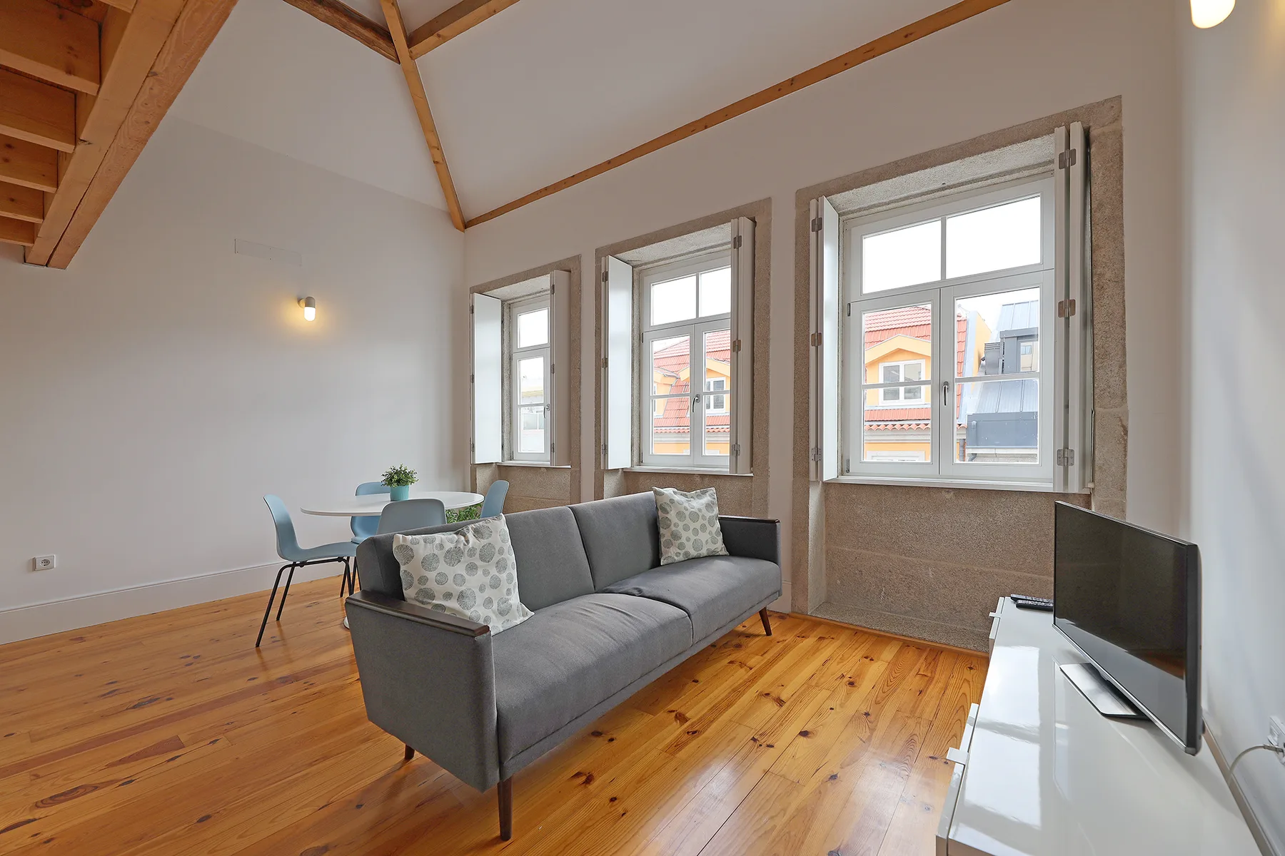 Una sala luminosa con asientos, un televisor y ventanas grandes.
