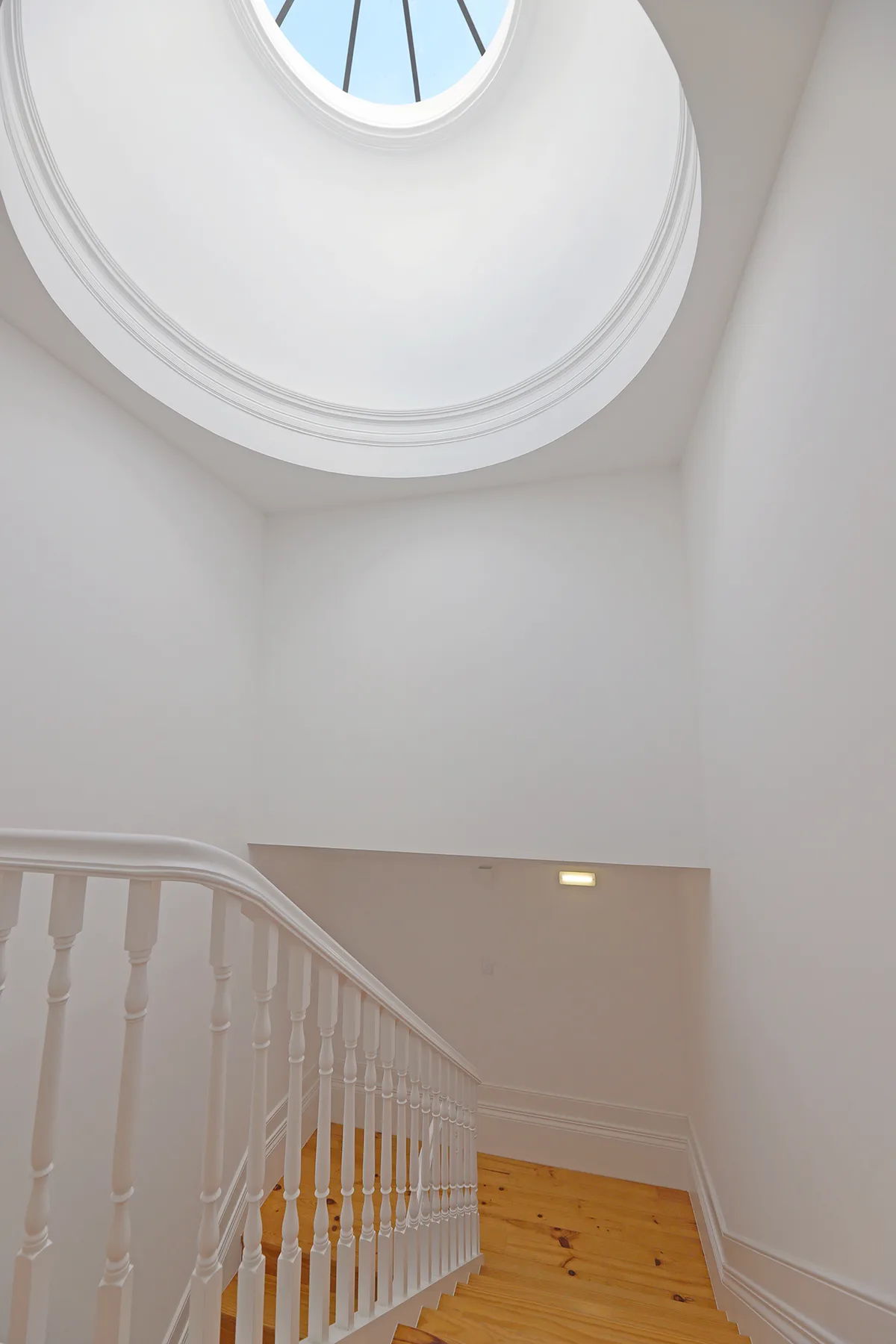 A bright stairwell with a round skylight above a wooden staircase.