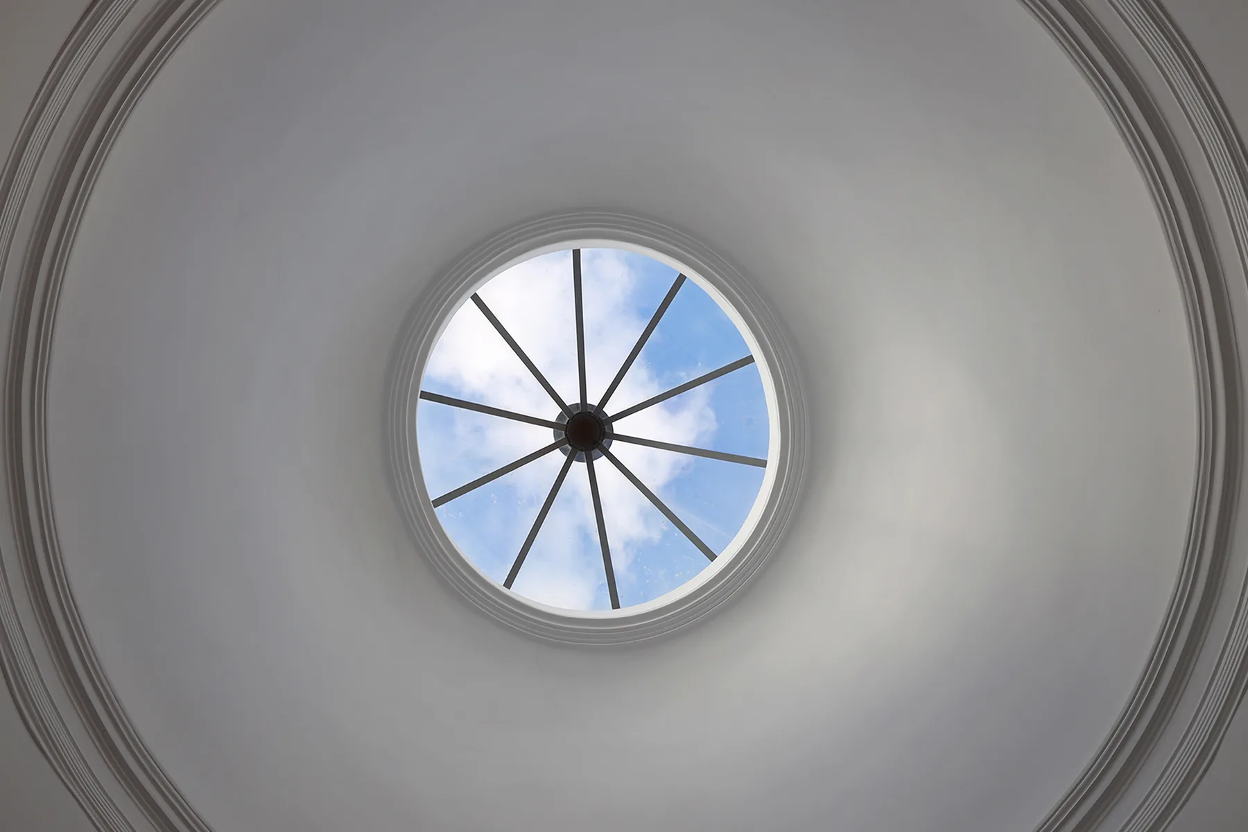 Un tragaluz circular con barras oscuras radiales está en un techo blanco.