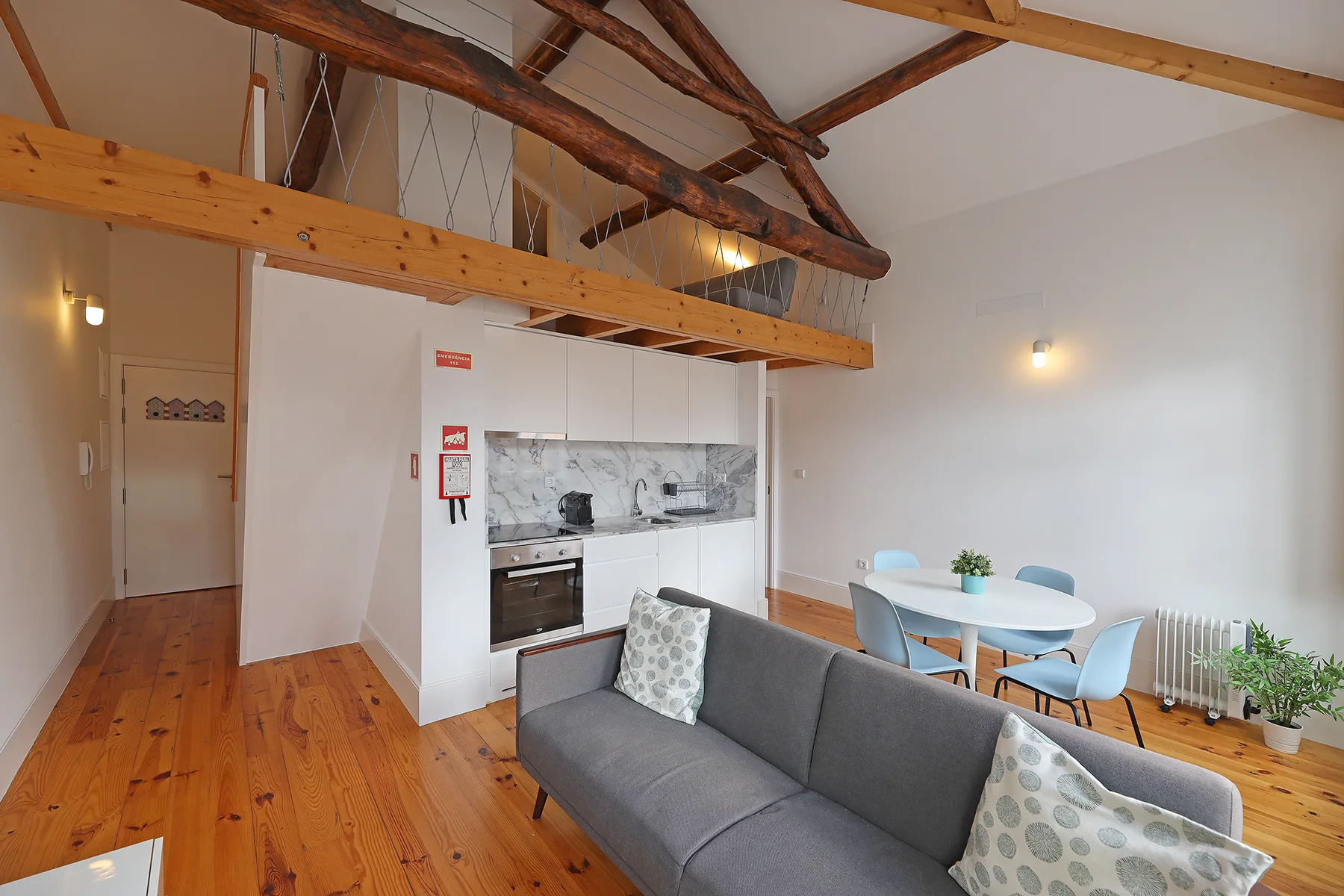 Sala de estar diáfana con sofá gris, mesa de comedor y cocina compacta.