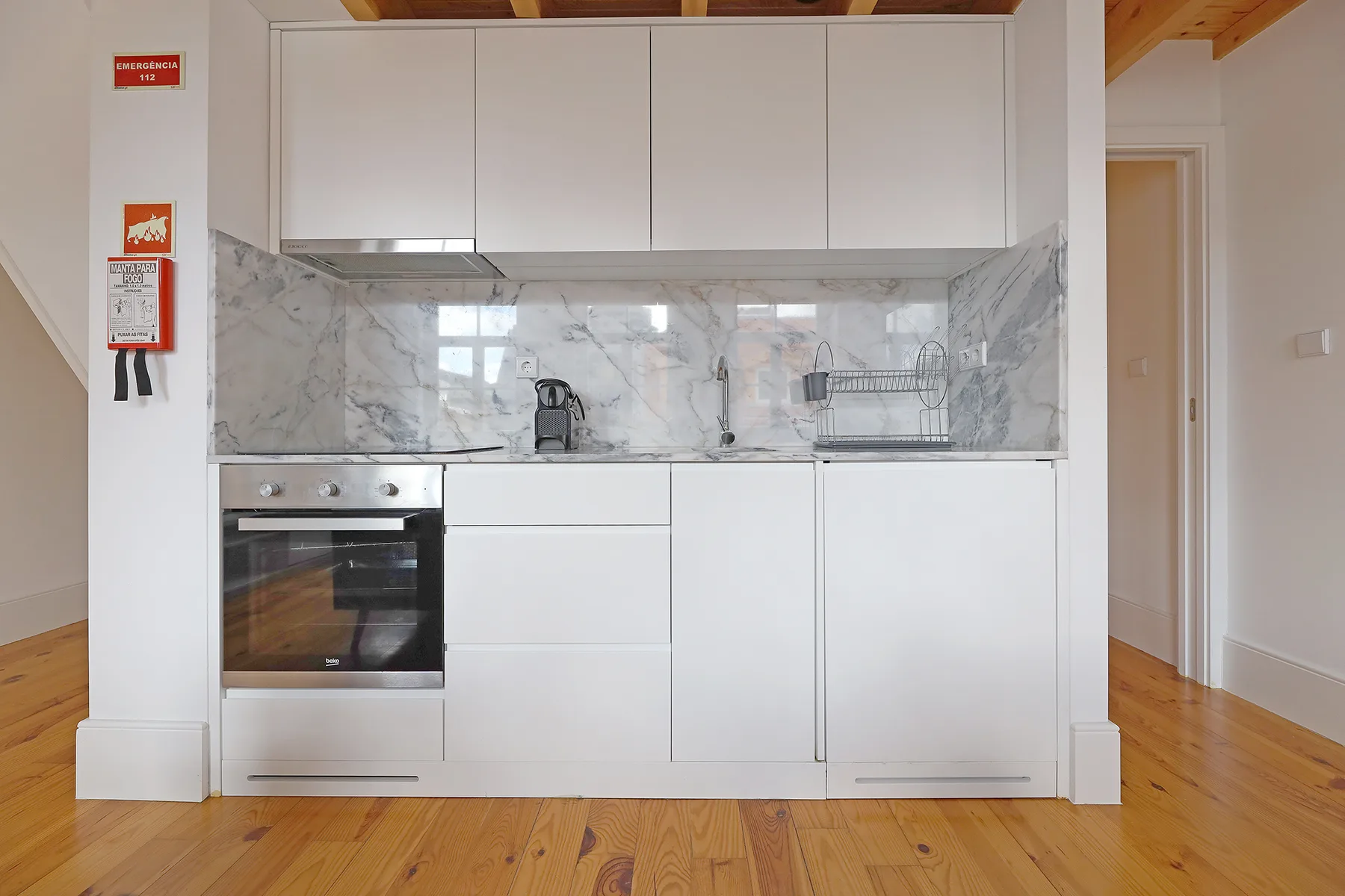 Una cocina compacta con armarios blancos, horno integrado y salpicadero de diseño marmoleado.