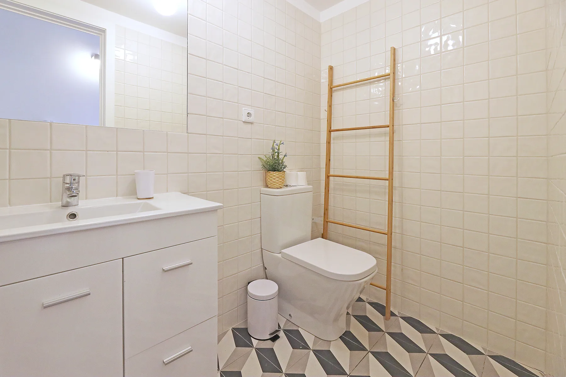 Un baño alicatado con lavabo, inodoro y una escalera de madera para toallas.